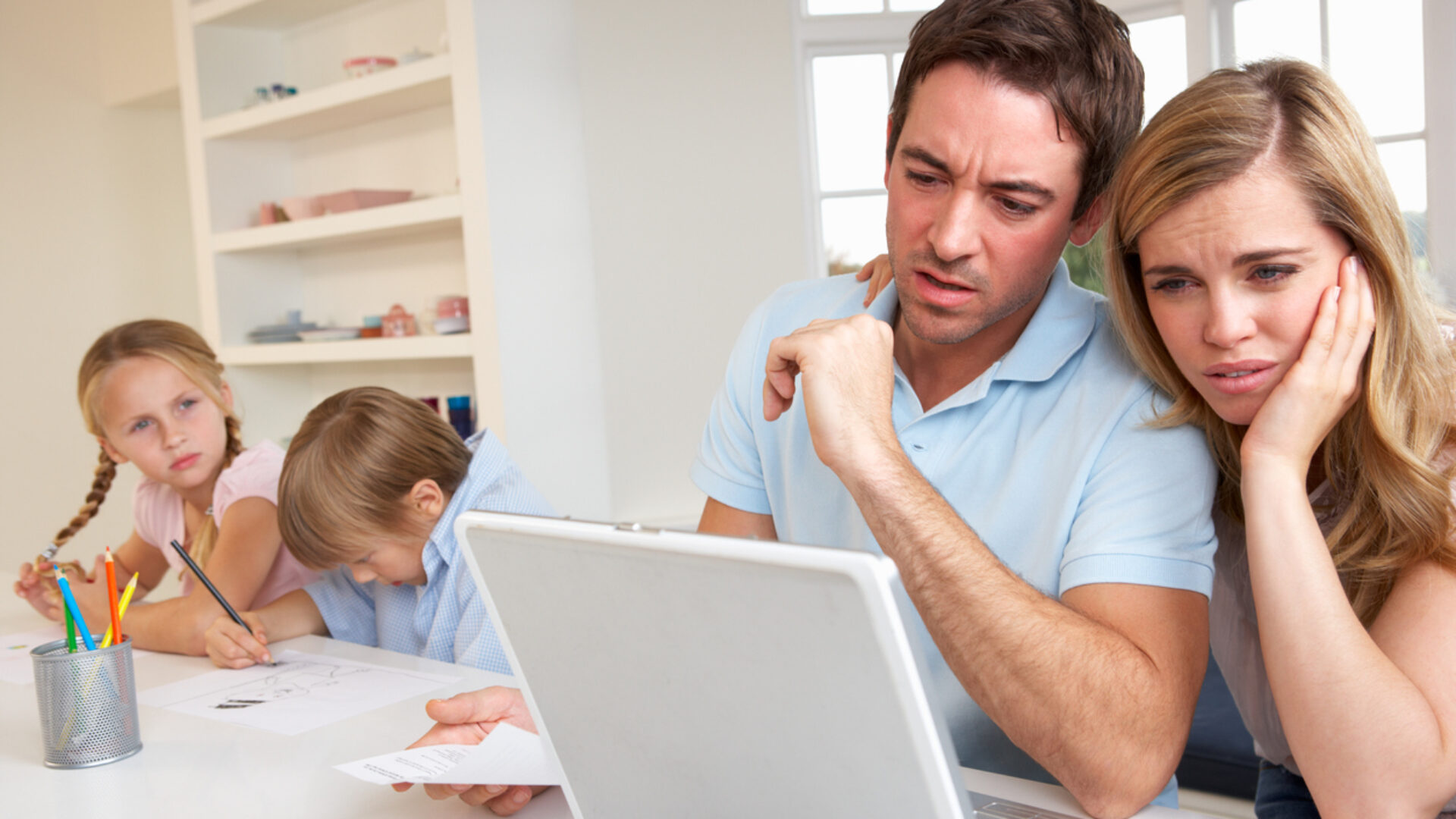 Young couple using laptop computer in kitchen looking conerned with children in background